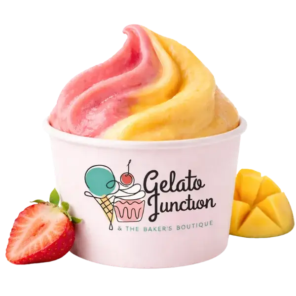A cup of swirled pink and yellow gelato from Gelato Junction, with a logo featuring an ice cream, cupcake, and cherry. Fresh strawberry and mango slices are placed beside the cup.
